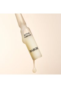Transparente Glasampulle, die eine blassgelbe Flüssigkeit enthält, beschriftet mit "ACTIVE PURIFIER" über dem Markennamen "BABOR", mit einem Tropfen, der sich an der Spitze bildet.