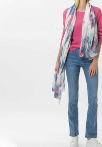 Sciarpa floreale leggera e fluente con motivi blu, rosa e bianchi. Indossata sopra un maglione rosa lavorato a maglia e jeans a zampa d'elefante blu, abbinata a scarpe bianche.