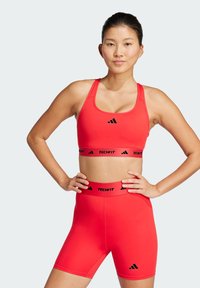 Rød atletisk crop top og høy midje shorts laget av strekkbart stoff. Har svart merkevare og elastiske bånd. Glatt tekstur, tettsittende design.