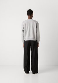 Grey sweatshirt with a relaxed fit and ribbed cuffs, paired with loose black pants. The background is plain and light.