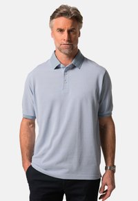 Jasnoniebieska koszulka polo z kontrastowym kołnierzykiem, krótkimi rękawami, trzema guzikami i teksturowanym materiałem. Uzupełniona zegarkiem na nadgarstku.