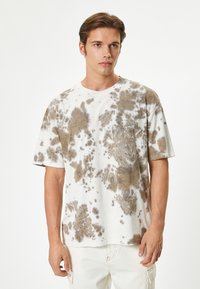 Kortærmet tie-dye t-shirt i hvid og brun. Har en afslappet pasform med rund halsudskæring og et blødt, tekstureret bomuldsstof.