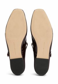 Scarpe con tacco alto in vernice bordeaux lucido, con una finitura liscia, dotate di una suola in gomma beige e un branding sottile sul fondo.