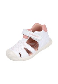 Sandalias infantiles blancas con acentos rosas, hechas de material sintético, con cortes, una correa de velcro y diseños decorativos en relieve.