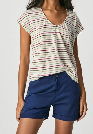 Femme portant un t-shirt à manches courtes rayé avec un col en V avec des lignes rouges, noires et beiges, assorti à un short bleu marine retroussé.
