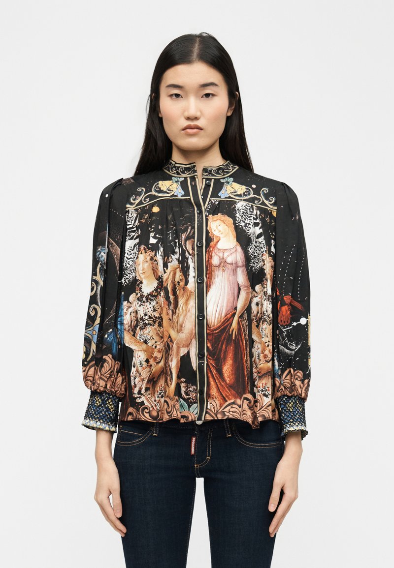 Femme portant un chemisier noir à manches longues avec un imprimé de style Renaissance représentant trois femmes en tenues classiques, et un jean foncé.