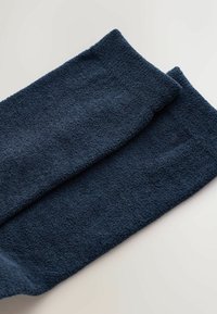 Granatowy ręcznik wykonany z miękkiego, puszystego materiału o gładkiej strukturze, starannie złożony na pół. Krawędzie wykończone czystym cięciem.