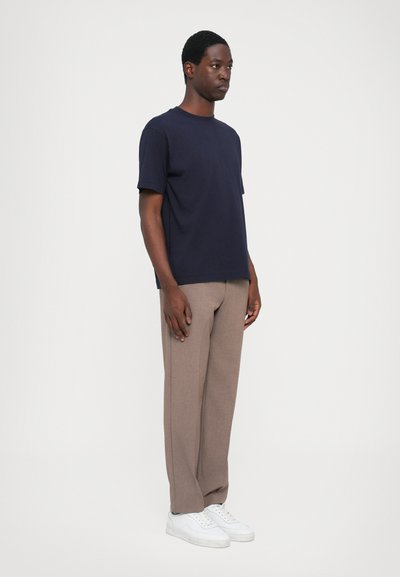 T-shirt en coton bleu marine à manches courtes, associé à un pantalon tapered beige clair et des baskets blanches, porté par une silhouette debout.