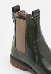 Botín de tobillo verde brillante con paneles elásticos laterales marrones, forro texturizado y tiradores. Cuenta con una suela resistente con agarre texturizado.