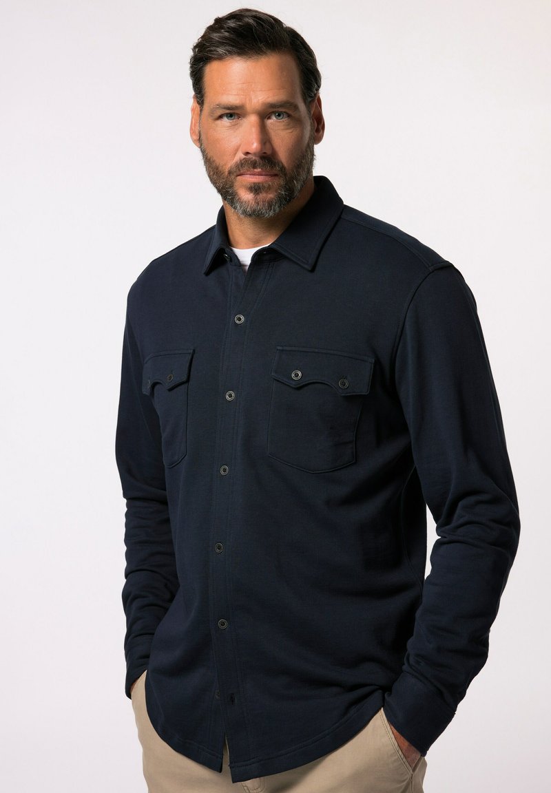 Camicia a maniche lunghe blu navy con bottoni frontali, due tasche sul petto e una texture semplice. Il colletto è strutturato, progettato per una vestibilità comoda.