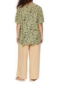 Blouse verte avec un motif floral noir, à manches courtes, coupe ample, portée avec un pantalon large beige. Texture de tissu lisse.