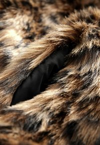Braun- und schwarzfarbiger Kunstpelzstoff mit einer weichen, strukturierten Oberfläche, die ein glattes schwarzes Futter darunter offenbart. Nahaufnahme der Fasern.