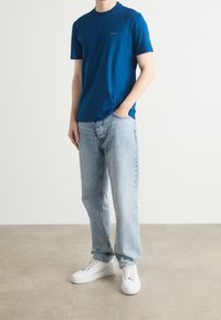 Modré bavlněné tričko s krátkým rukávem a kulatým výstřihem, spárované se světle modrými džíny a bílými teniskami. Jednoduchý design, pohodlný střih.