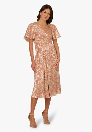 Roze bloemenjurk met gouden details, V-hals, flottende mouwen en een vloeiende rok. Gedirigeerd met naaktkleurige hoge hakken sandalen.