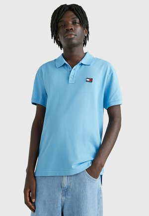 Polo de color azul claro en material de algodón, con una tapeta de tres botones, mangas cortas y un pequeño logo bordado en el lado izquierdo del pecho.