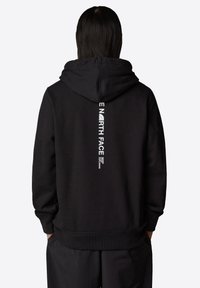 Svart hoodie med en stor logotyp på ryggen i vit text. Mjuk, strukturerad tyg med en avslappnad passform och ribbade muddar och nederkant.