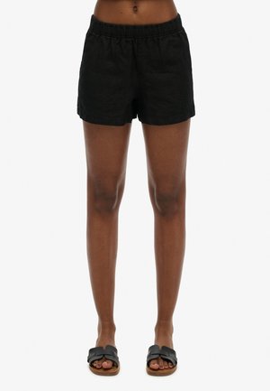 Shorts en lin noir avec une taille élastique, présentant une coupe décontractée et un design minimaliste. Associés à des sandales noires à glisser.