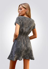 Vestido corto de manga corta en blanco y negro con una cintura ajustada y un dobladillo acampanado, que presenta un patrón moteado y una textura de tela suave y fluida.