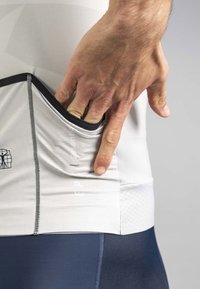 Fitted athletic shirt in white with a textured pattern, featuring a side pocket accessed by a hand. Dark blue leggings complement the design.