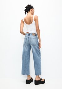 Helle blaue weit geschnittene Jeans aus Denim mit einem rohen Saum und Gesäßtaschen. Getragen mit einem weißen Tanktop und schwarzen Plateausandalen.