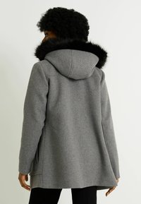 Abrigo de mezcla de lana gris con capucha que cuenta con un borde de piel sintética negra. El diseño incluye bolsillos laterales y un corte relajado para mayor comodidad.