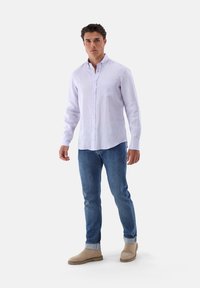 Helles lila Leinenhemd mit Button-Down-Kragen, Brusttasche und langen Ärmeln. Kombiniert mit blauen Denim-Jeans und hellbraunen Ankle-Boots.