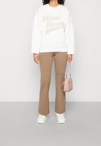 Vit sweatshirt med "Miami Sports" i beige, tillsammans med ljusbruna utsvängda byxor och vita sneakers. Tillbehören inkluderar en liten rosa väska.