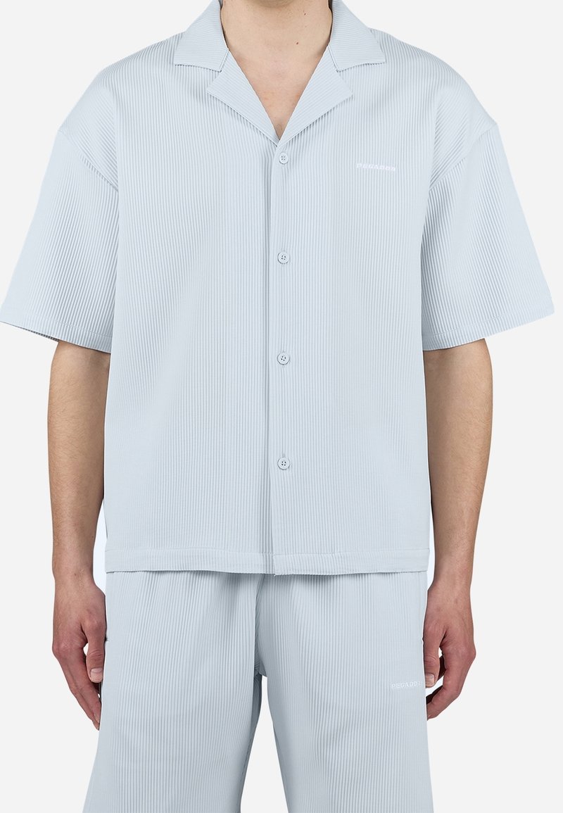 Homme portant une chemise bleu clair à manches courtes boutonnée et un short assorti avec de subtils plis verticaux.