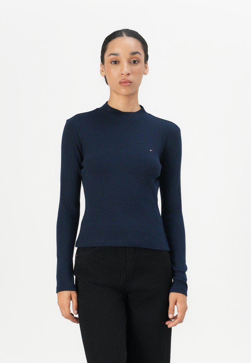 Maglia a maniche lunghe blu navy realizzata in cotone con un design aderente e un collo alto; presenta un piccolo logo sul petto; abbinata a pantaloni neri.