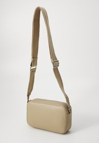 Borsa a spalla rettangolare beige con superficie liscia, tracolla in tessuto regolabile e chiusura con zip, caratterizzata da un sottile logo circolare sul lato.