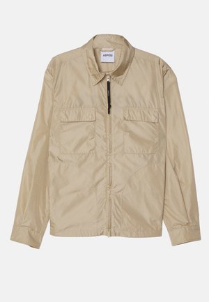 Giacca leggera beige con colletto a punta, due tasche sul petto, chiusura frontale con zip e orlo inferiore elasticizzato. Tessuto liscio e testurizzato.