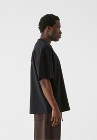 Sort oversized t-shirt med korte ærmer, rund udskæring og afslappet pasform. Stoffet ser glat ud med en let glans.