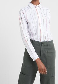 Witte overhem shirt met verticale gekleurde lijnen in roze, blauw en goud; gecombineerd met olijfgroene, gestructureerde cargo broeken.