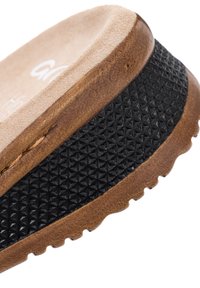 Nærbillede af en brun sandalsål med struktureret sort gummigreb og beige polstret indersålskant.