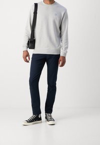 Szara bluza z okrągłym dekoltem i małym logo, granatowe spodnie oraz czarne trampki Converse z białymi podeszwami i sznurówkami, noszone z czarną torbą.