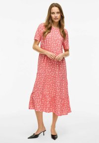Robe midi florale rose à manches courtes, design à volants et coupe décontractée. Tissu lisse avec une texture légère et aérée. Mules à talons noires.