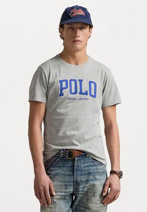 Gray cotton t-shirt with blue "POLO" text, paired with distressed blue jeans and a blue baseball cap featuring red logo. Brown belt with circular buckle.