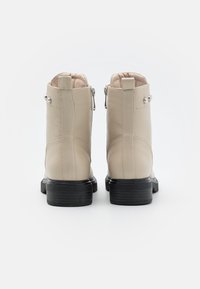 Beige leather ankle boots with a smooth texture, featuring side zippers and silver accent studs, on a black sturdy sole.