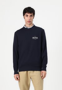Marineblauwe katoen sweatshirt met lange mouwen, ronde hals en geborduurde "HILFIGER" logo op de borst; gladde textuur en ribbelboorden.