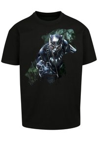 Juodas trumpomis rankovėmis marškinėliai su superherojaus grafiką juodu kostiumu ir aštriais nagais, ant tekstūruoto žalio fono.