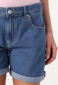 Jeans šortsi z zavitkom, v svetlo modri barvi, z oprijetim pasom in sprednjim žepom s srebrnim gumbom.