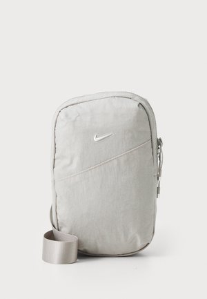 Compact light gray Nike crossbody bag with front zipper pocket and adjustable strap, shown upright against white background.
