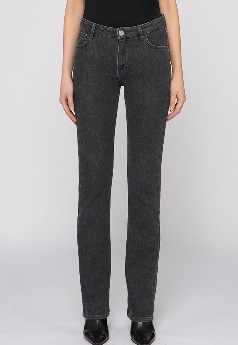 Jeans de mezclilla negra con corte ajustado, cinco bolsillos y cierre de botón. Textura suave y detalle de costura mínima.