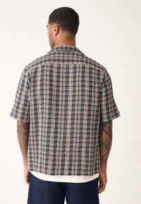 Chemise à manches courtes présentant un motif à carreaux en marine, crème et beige. Confectionnée en tissu texturé avec une coupe décontractée et un col.