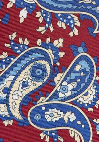 Punainen kangas, jossa on monimutkaisia sinisiä paisley- ja kukkakuoseja, joissa on beige ääriviivat ja teksturoitu kudonta. Huomattava elävä värikontrasti.