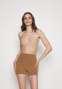 Naakt, gepolsterde beha met verstelbare banden, gecombineerd met bruine naadloze high-waisted shorts. Beide items hebben een gladde textuur en een aansluitend ontwerp.