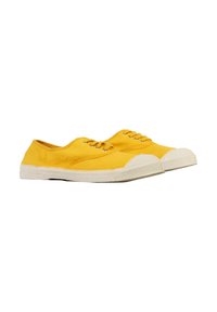 Un par de zapatillas de lona amarillas con suelas de goma blanca y punteras blancas, atadas, colocadas una al lado de la otra sobre un fondo blanco.