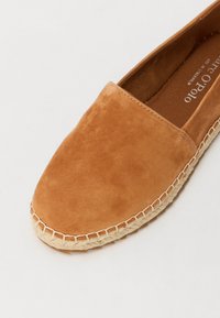 Espadrille en suède marron avec un bout rond et une semelle en raffia tressé. Présente un bord cousu et une texture lisse sur le dessus.