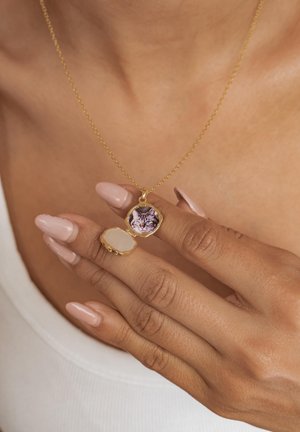 Gold locket necklace held open by hand with light pink nails, revealing a small photo of a kitten inside.