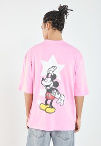 Rosa oversized t-skjorte med korte ermer, med en tegneserie-design av Mikke Mus og hvite stjernemønstre på baksiden.